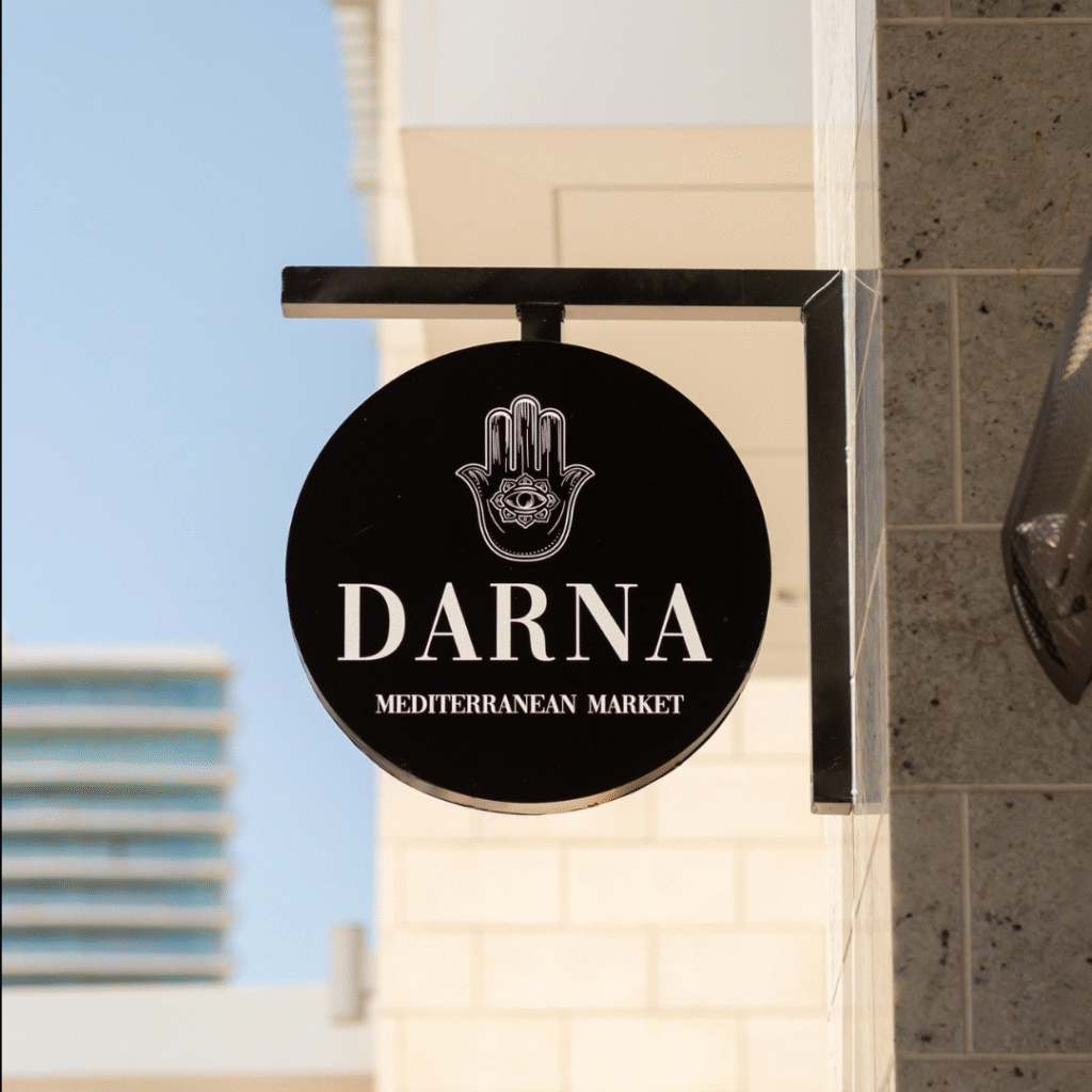 Black circular Darna sign with white lettering and Hamsa logo mounted on exterior wall.