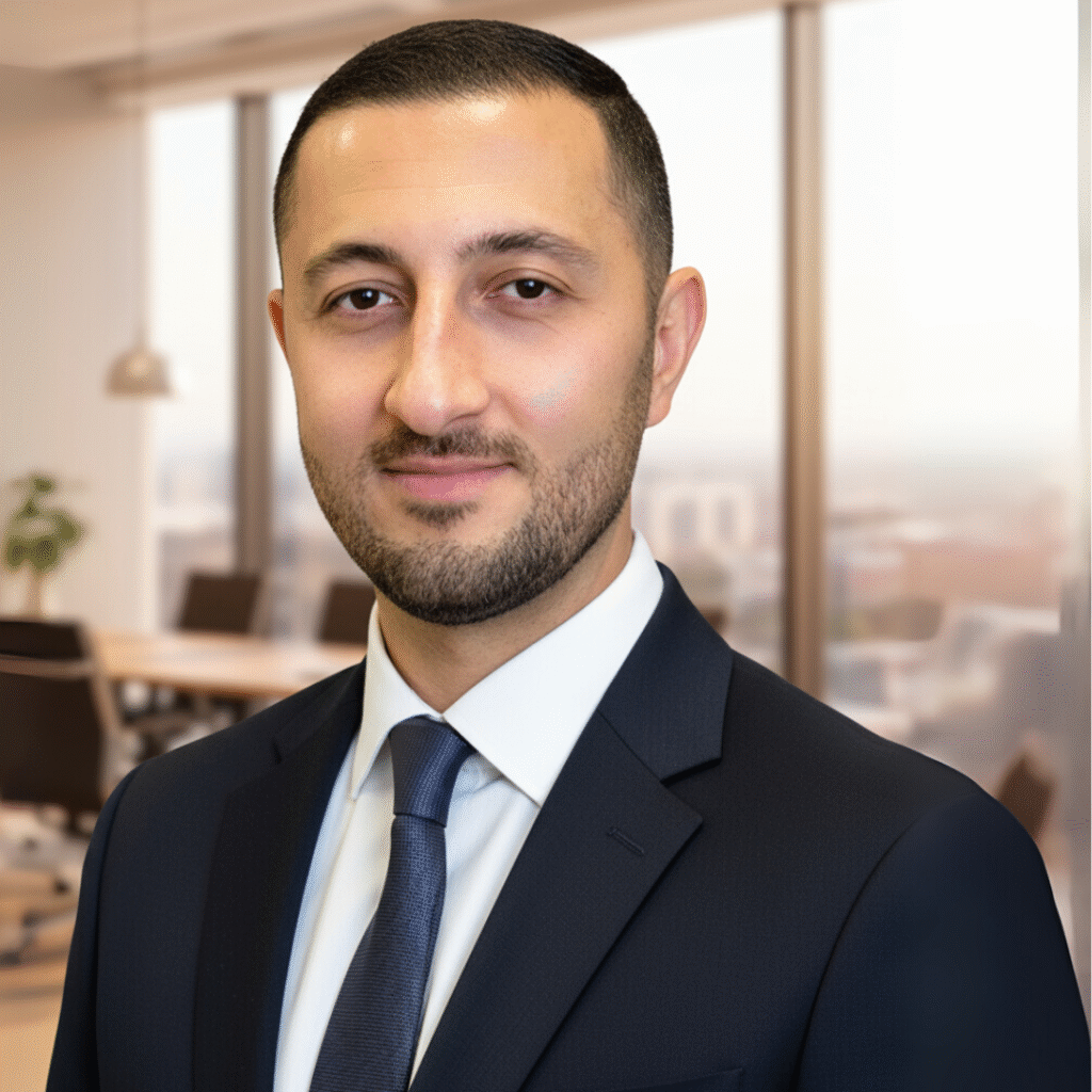 Professional headshot of Shawn Zafarpour in a dark suit and tie, posed in a bright office with blurred background.