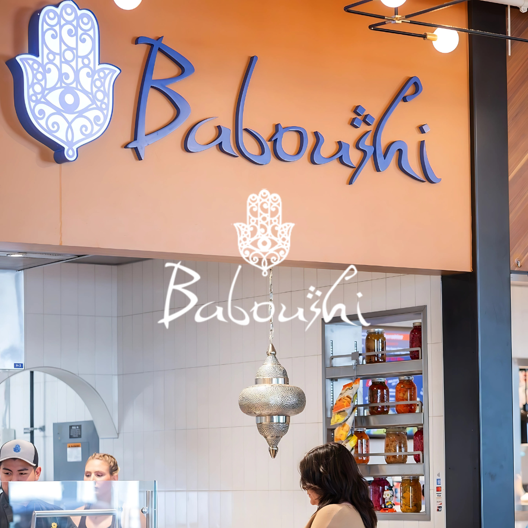 Baboushi storefront inside The Exchange Food Hall, featuring the blue Hamsa hand symbol, logo signage, and Mediterranean décor.