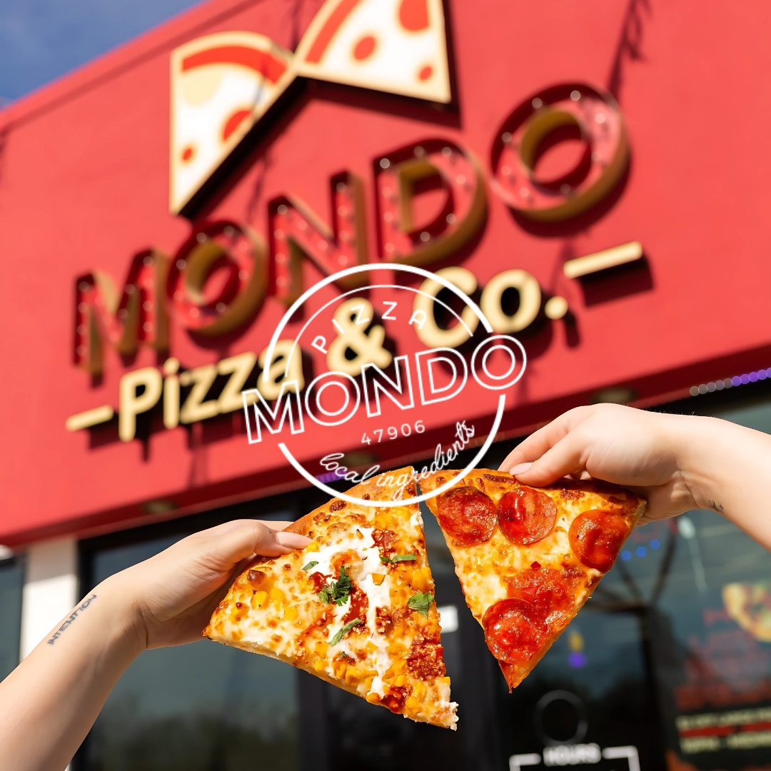 Two pizza slices held in front of Mondo Pizza Co. red storefront.